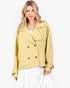 A woman modeling a cropped, double-breasted blazer in a light mustard yellow color, styled with a white top and white skirt against a plain white studio background.