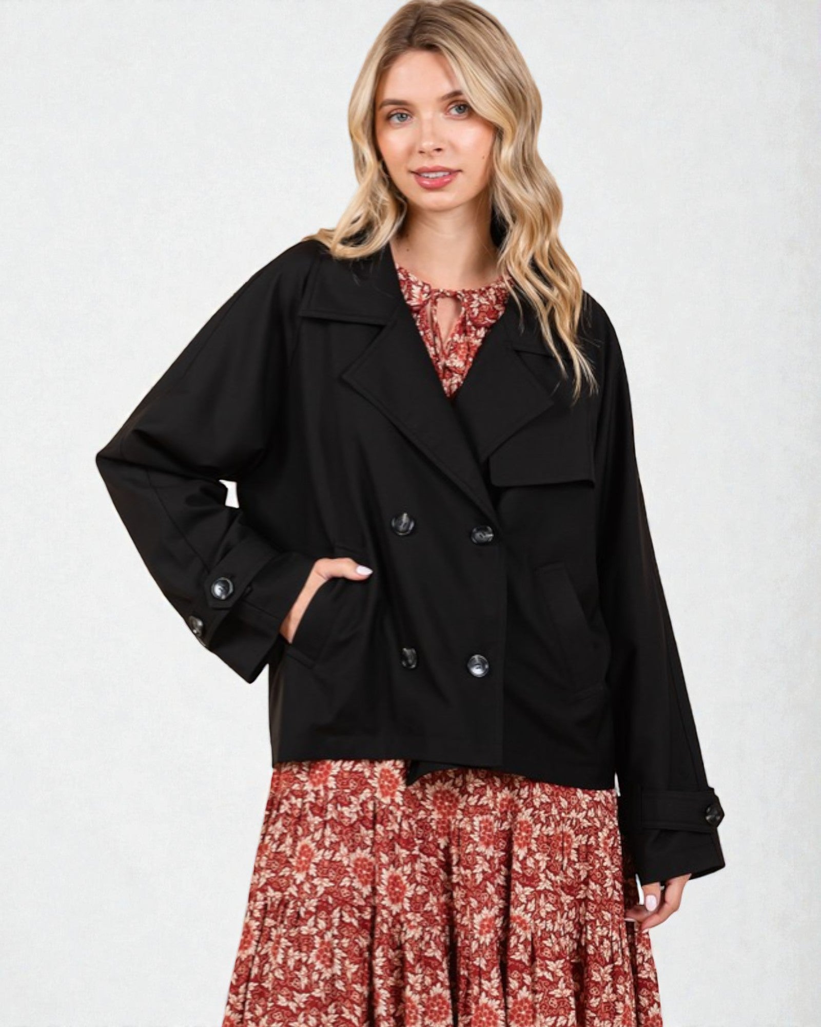 Woman wearing a black coat over a floral dress on a white background