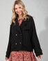 Woman wearing a black coat over a floral dress on a gray background