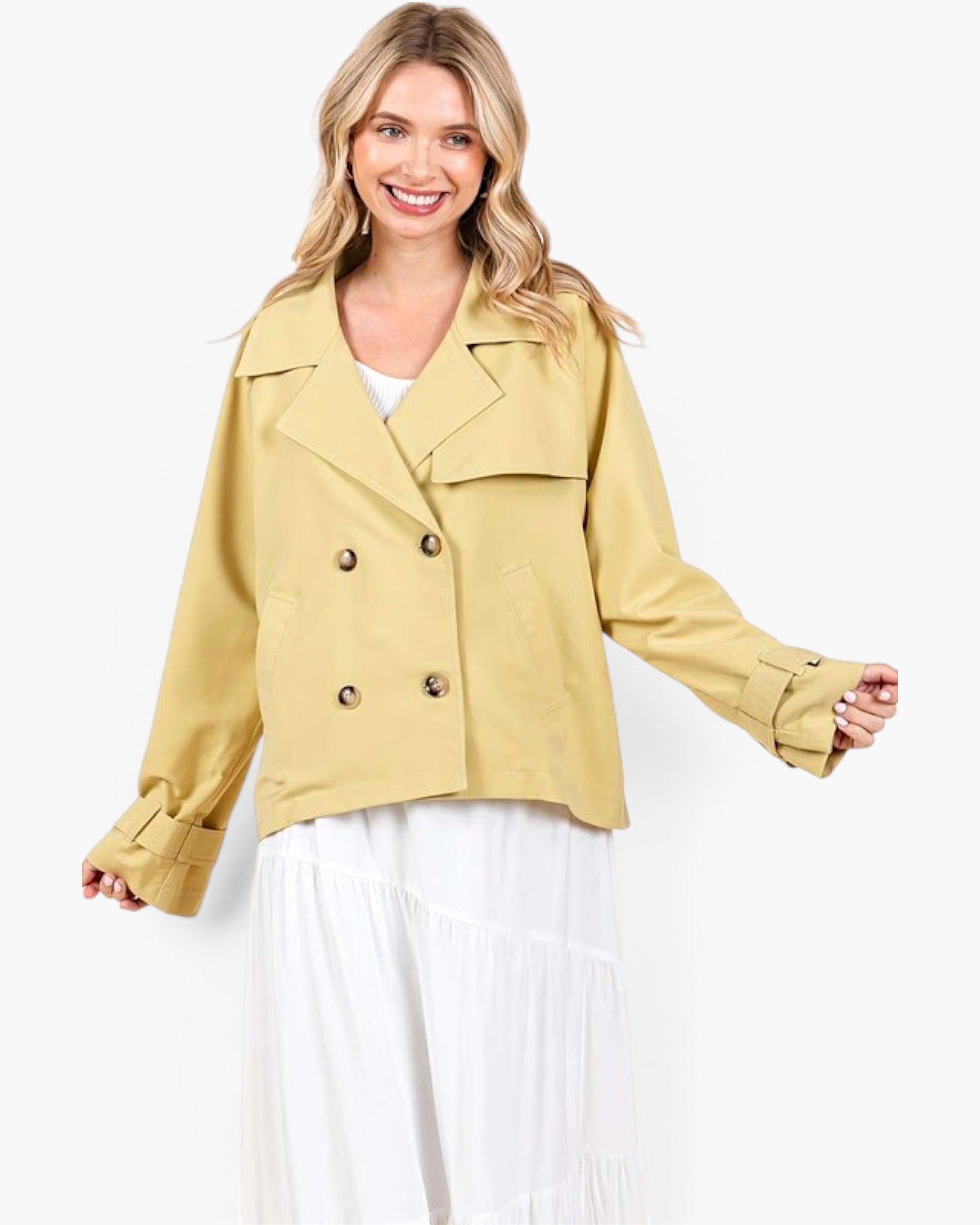 A woman modeling a cropped, double-breasted blazer in a light mustard yellow color, styled with a white top and white tiered maxi skirt against a plain white studio background.