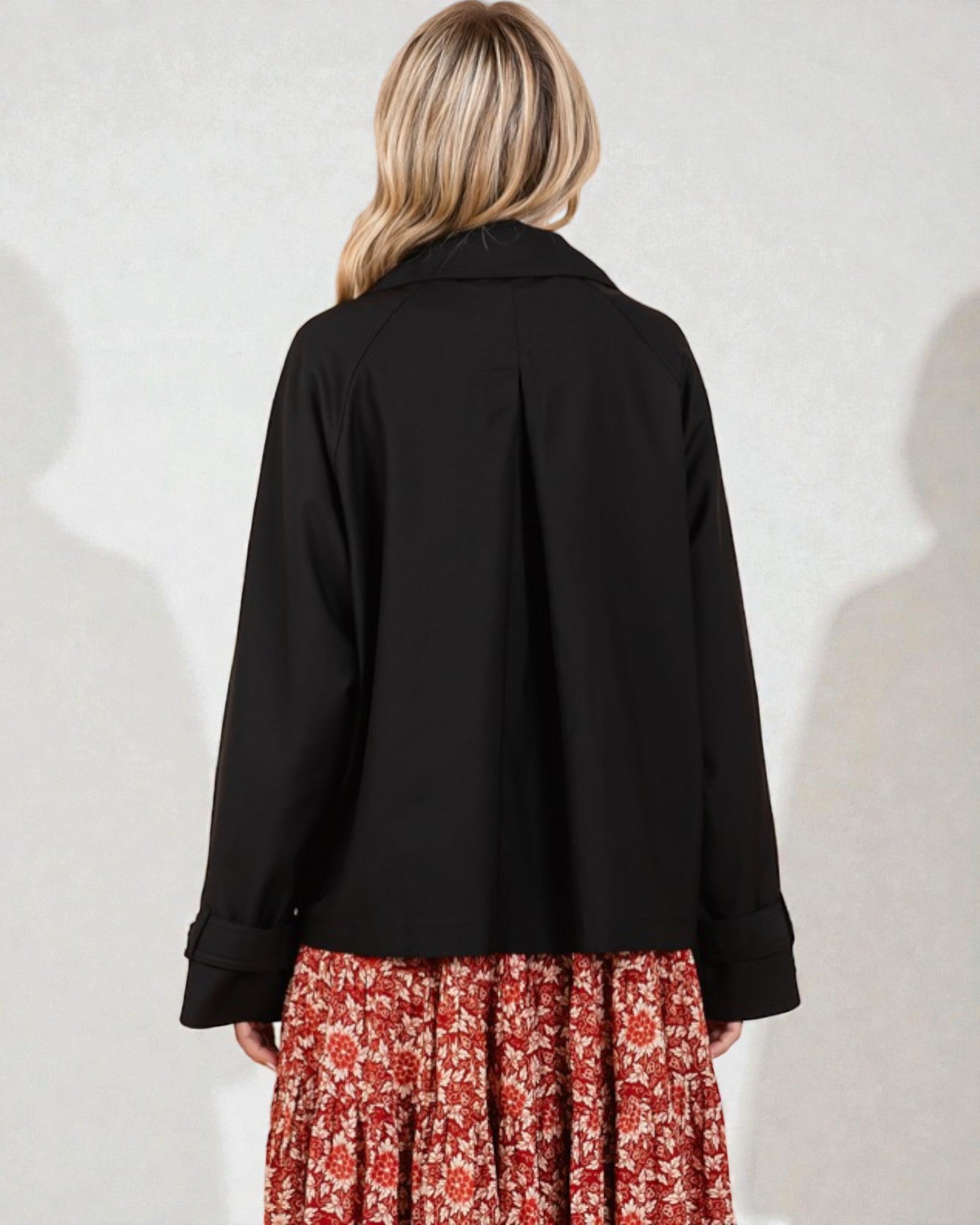 Person wearing a black coat over a floral dress on a white background
