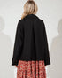 Person wearing a black coat over a floral dress on a white background