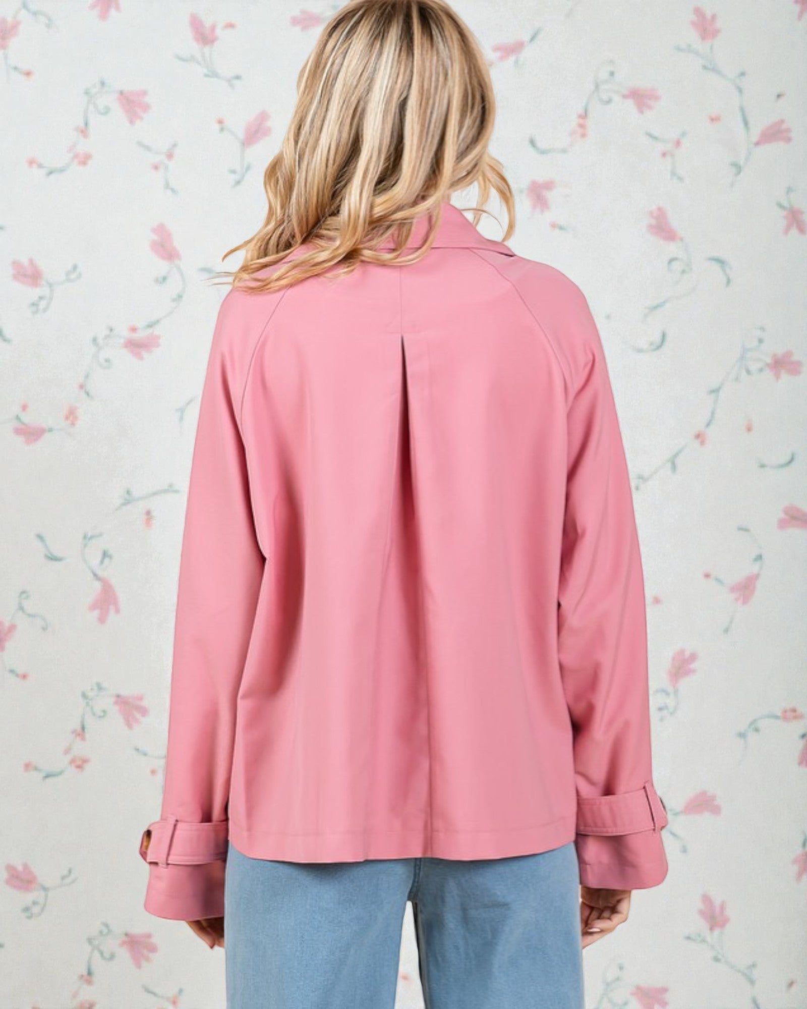 Person wearing a pink jacket with floral wallpaper background