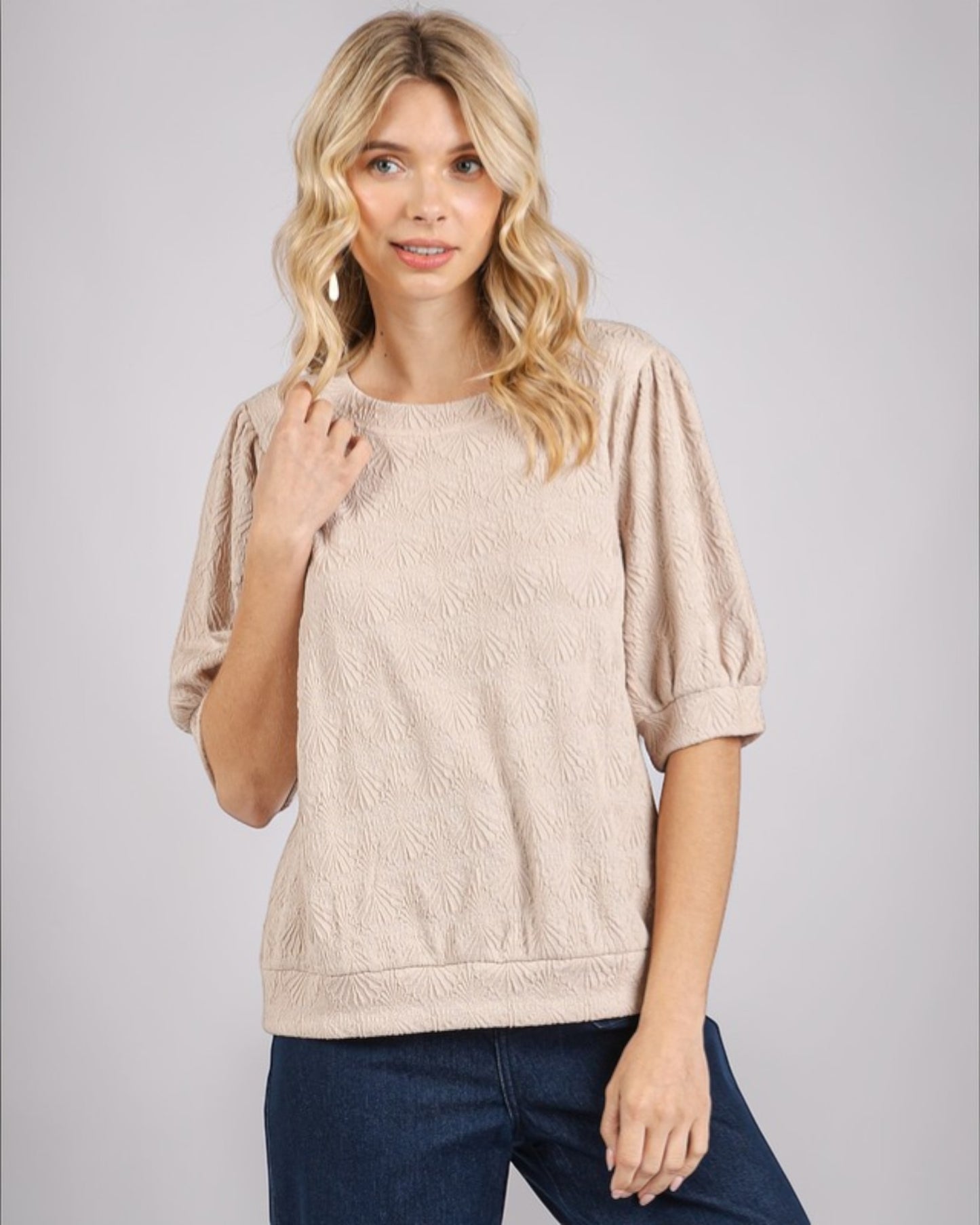 Woman wearing a beige cable knit sweater and blue jeans on a gray background