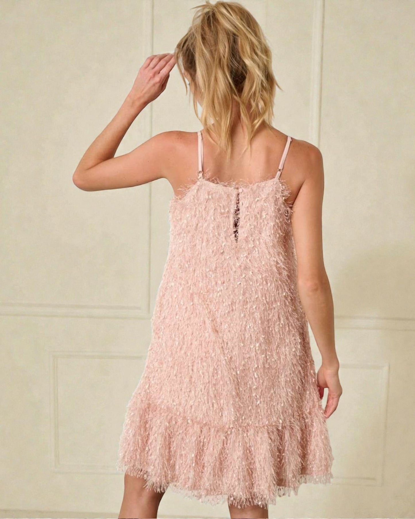 Woman wearing a pink fringed dress against a neutral background