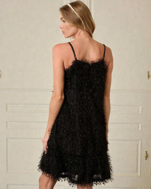 Woman wearing a black lace dress against a white wall.