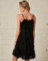 Woman wearing a black lace dress against a white wall.