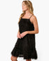 A woman wearing a black textured spaghetti-strap mini dress with a flared, feather-like skirt, posed against a solid white background.