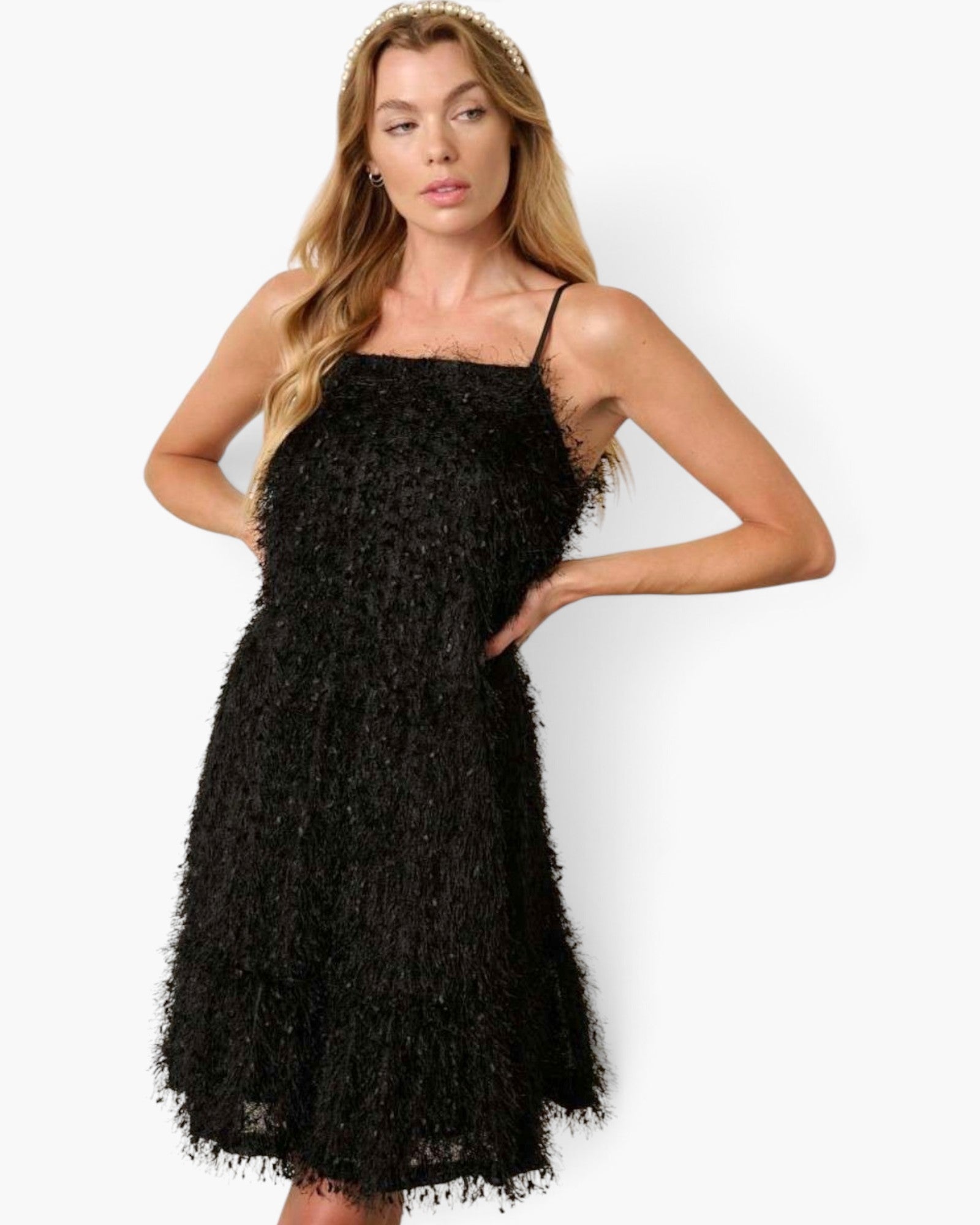A woman modeling a black textured spaghetti-strap mini dress with a fringed hem against a plain white studio background.