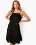 A woman modeling a black textured spaghetti-strap mini dress with a fringed hem against a plain white studio background.