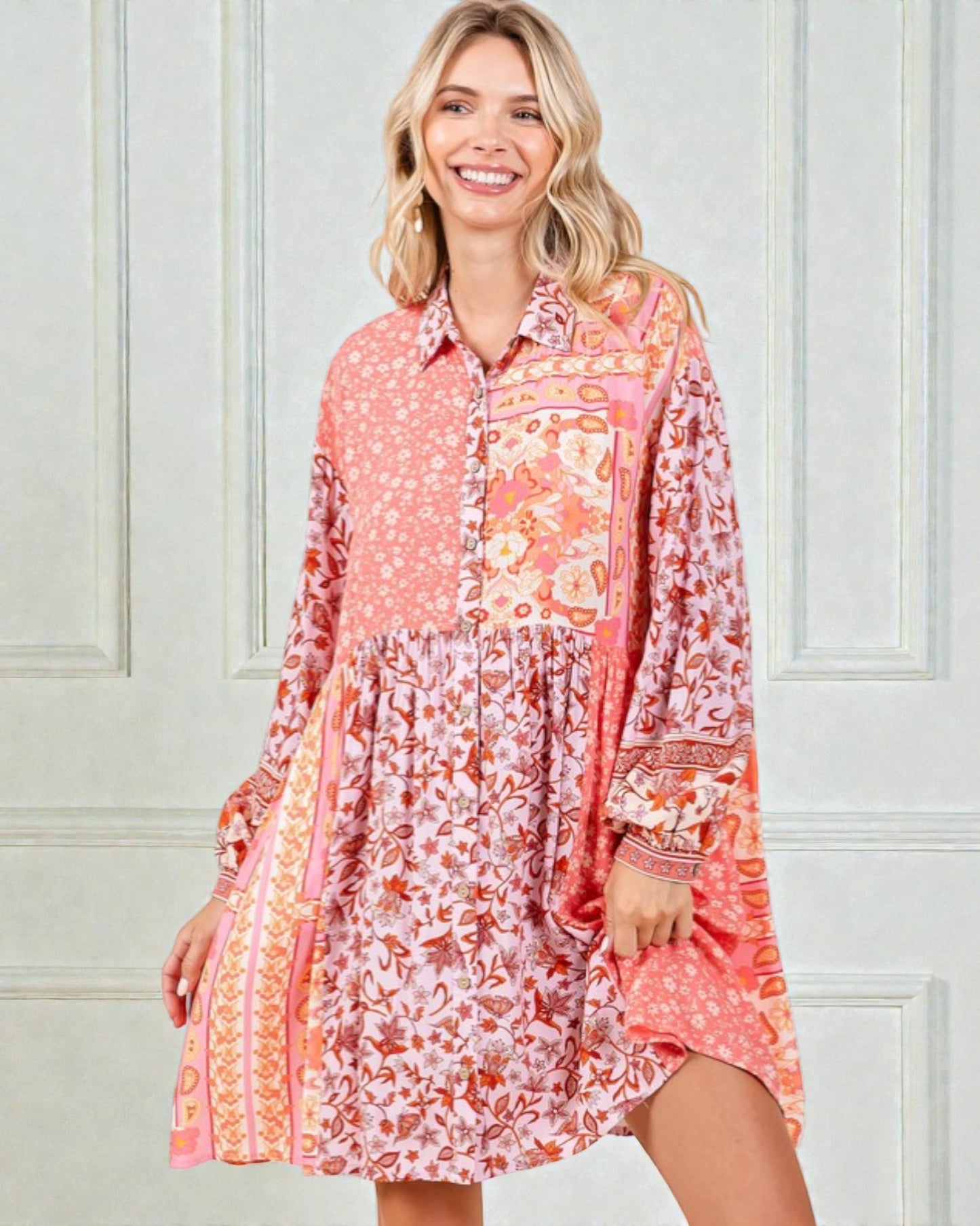 Woman wearing a long-sleeve, patterned dress against a light-colored wall.