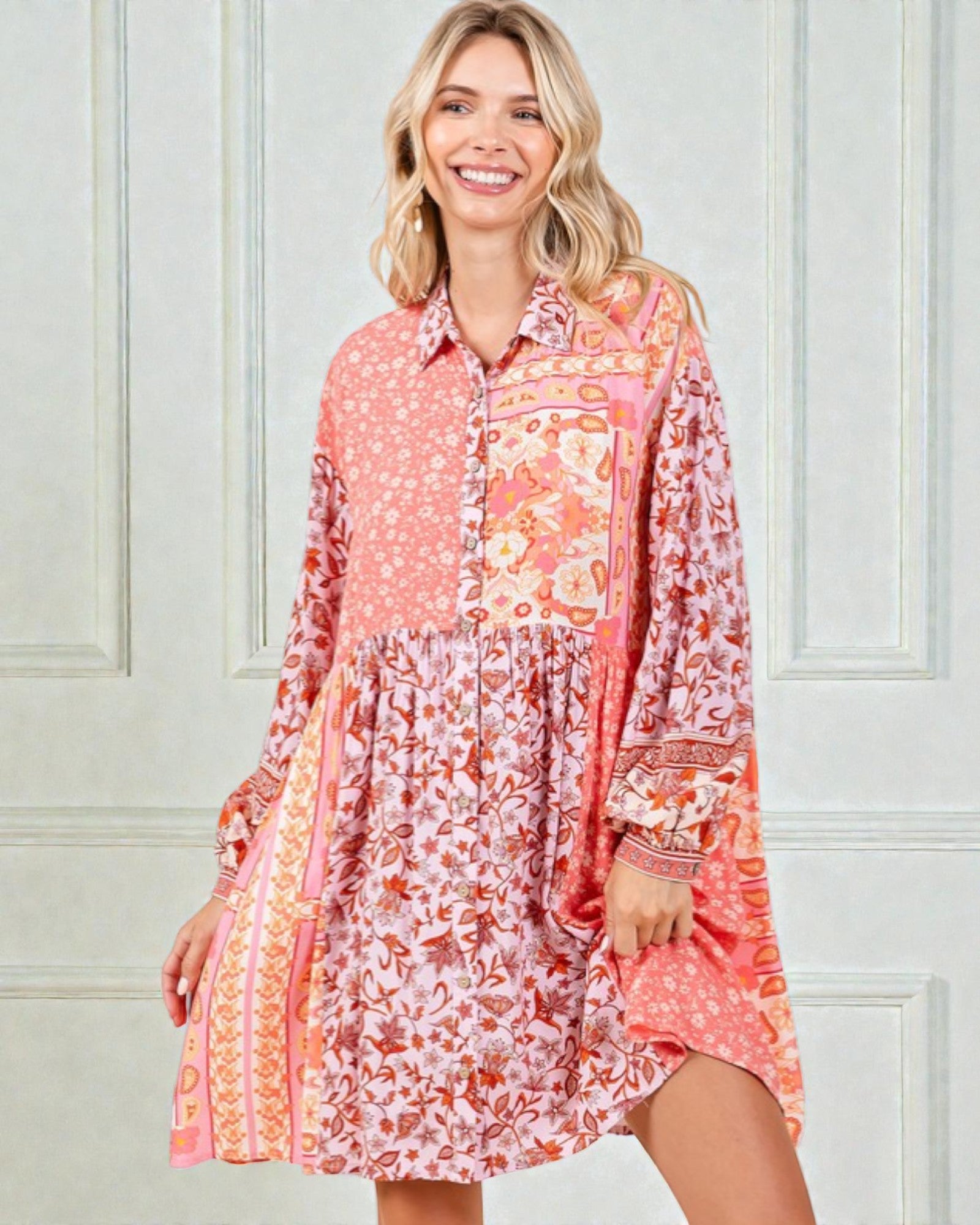 Woman wearing a long-sleeve, patterned dress against a light-colored wall.