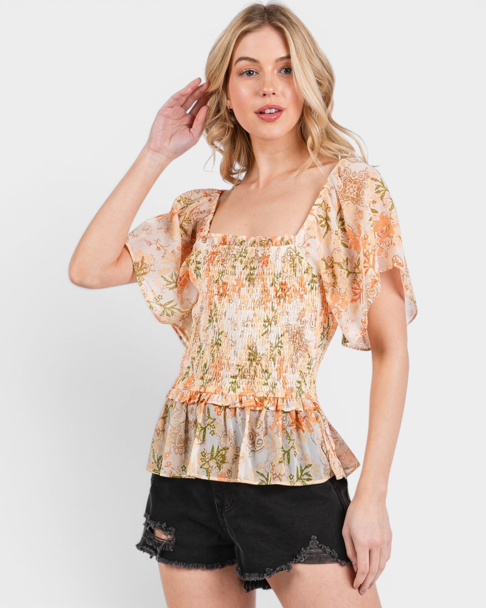 Woman wearing a floral blouse and black shorts on a white background