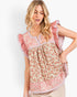 A woman wearing a short-sleeve bohemian-style top with a pink and beige floral print, ruffled sleeves, and a split neckline, paired with beige pants against a light gray studio background.