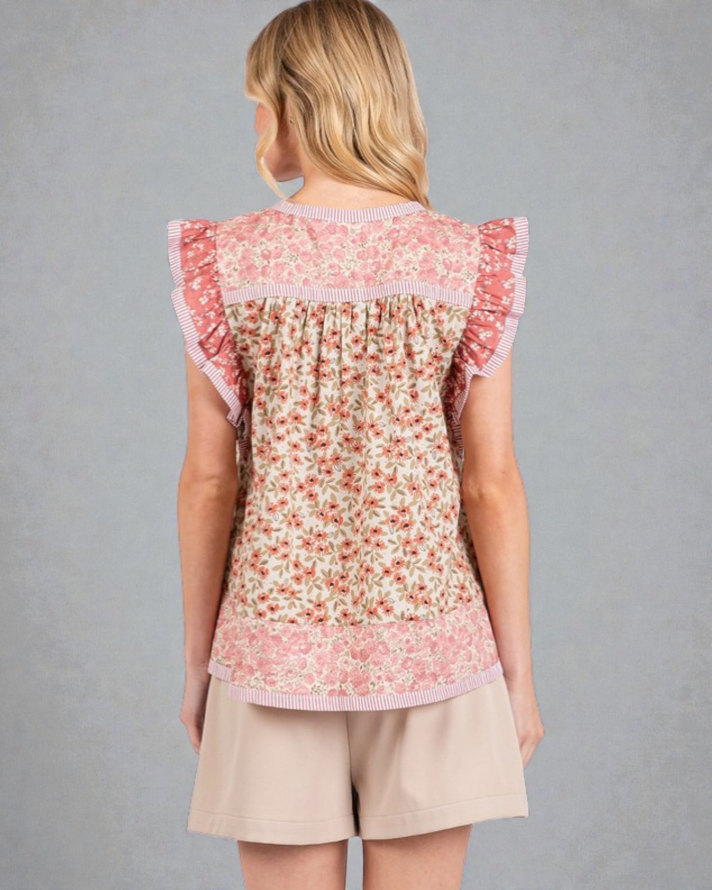 Woman wearing a floral top and beige shorts against a gray background