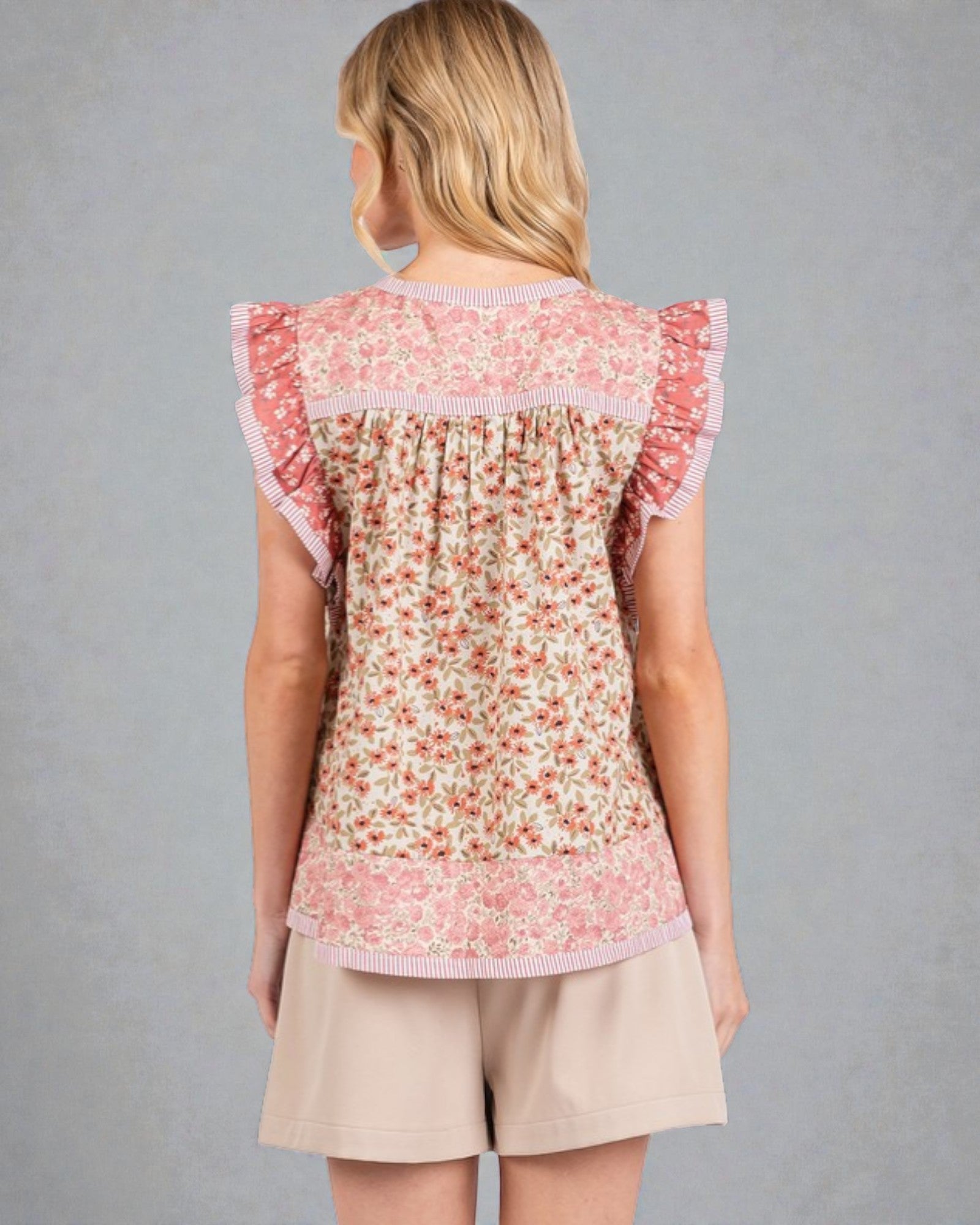 Woman wearing a floral top and beige shorts against a gray background