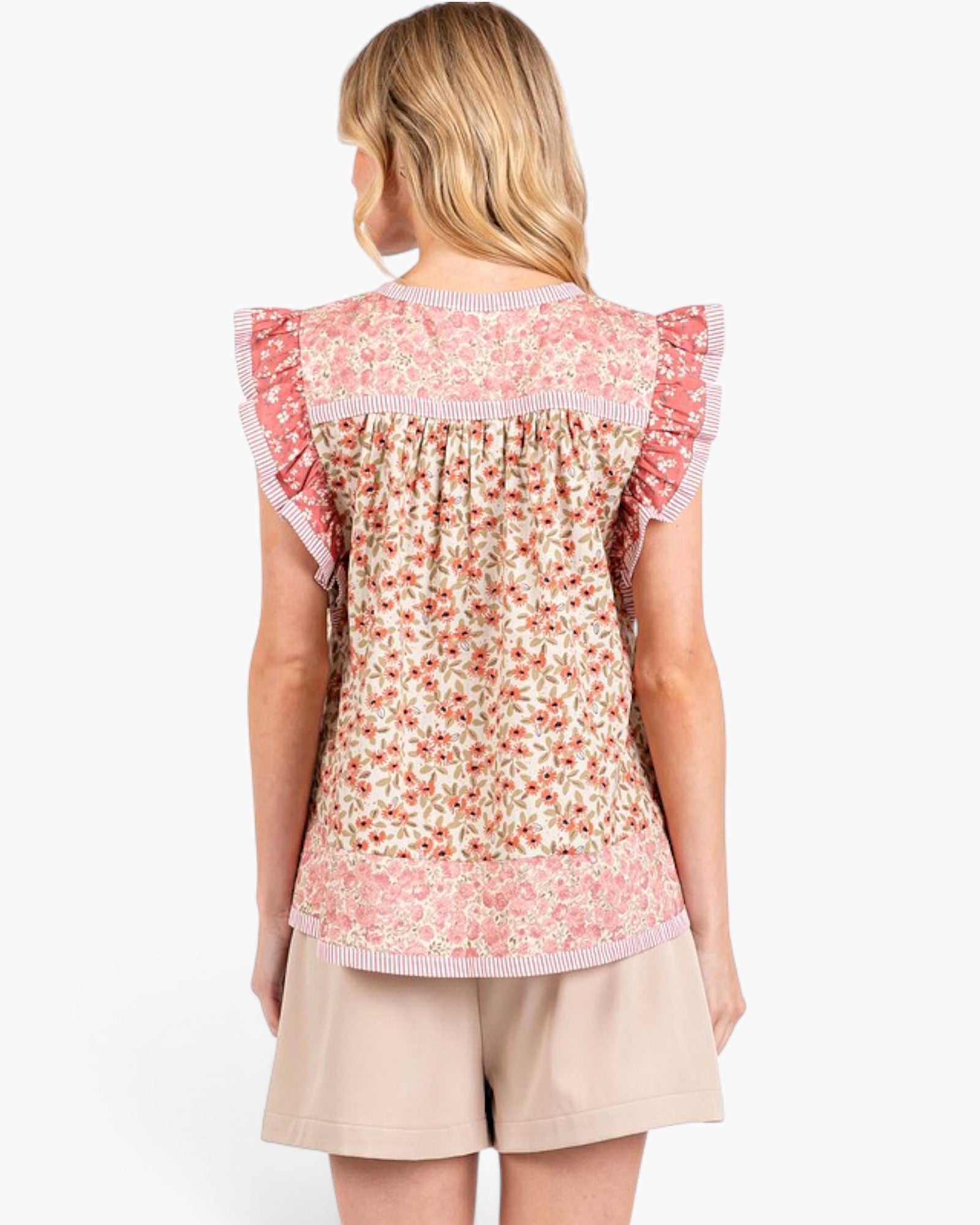 A woman shown from the back wearing a floral ruffled top and beige shorts against a plain white studio background.