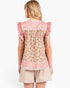 A woman shown from the back wearing a floral ruffled top and beige shorts against a plain white studio background.