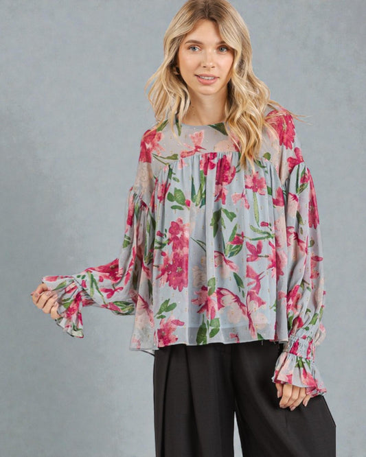 Woman wearing a floral blouse with long sleeves against a gray background