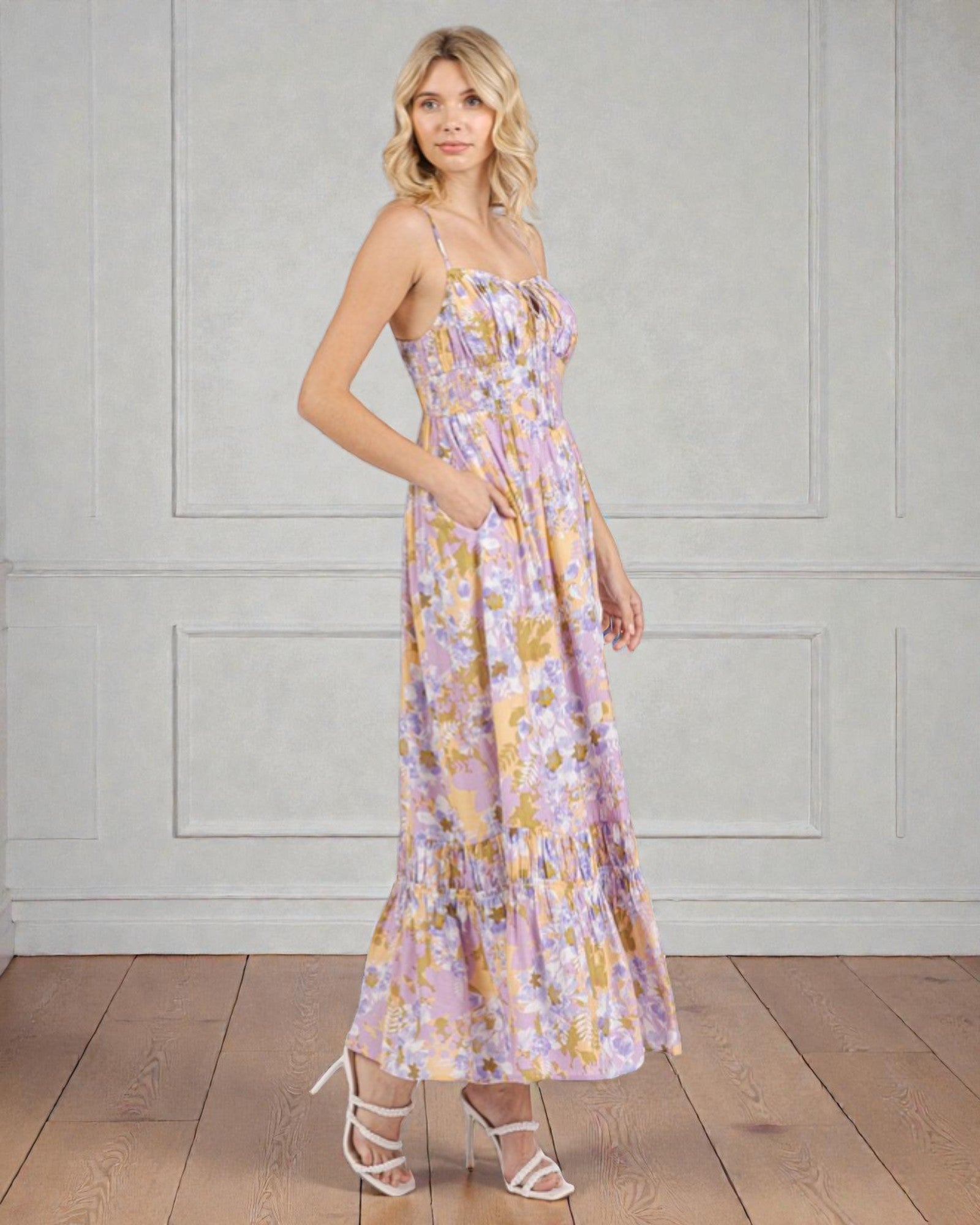 Woman wearing a floral dress standing against a plain wall.