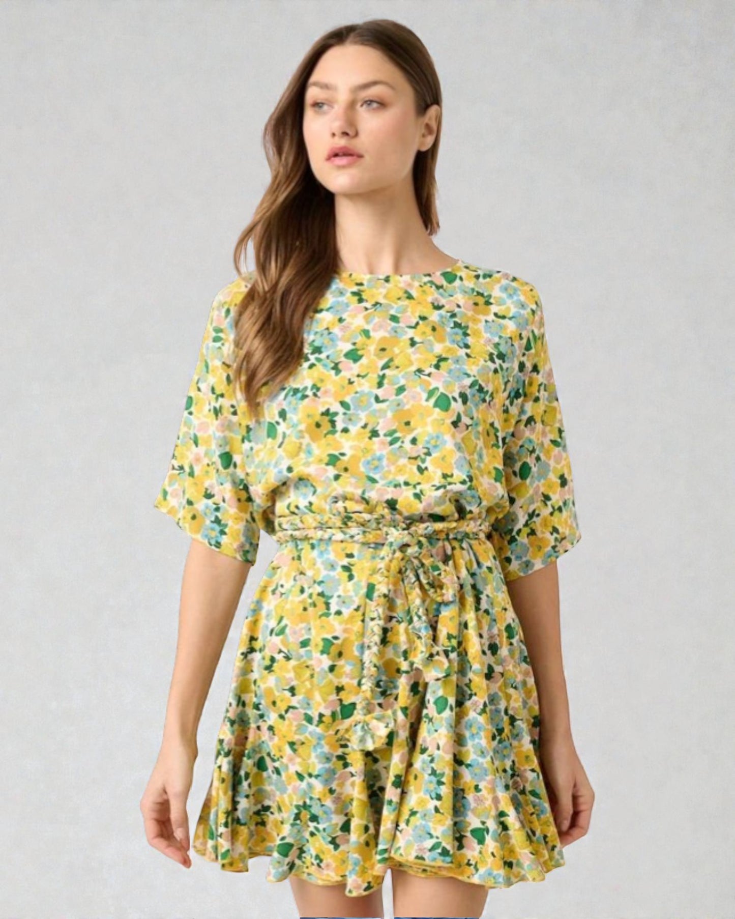 Woman wearing a yellow floral dress against a gray background