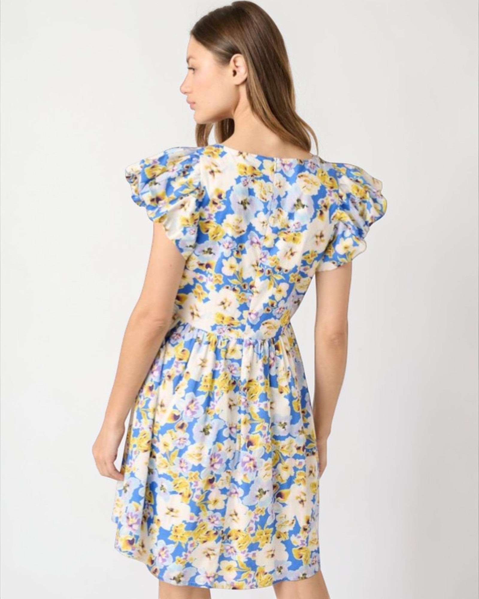 Woman wearing a floral dress with blue, yellow, and white colors on a plain background