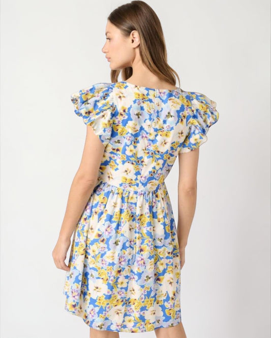 Woman wearing a floral dress with blue, yellow, and white colors on a plain background