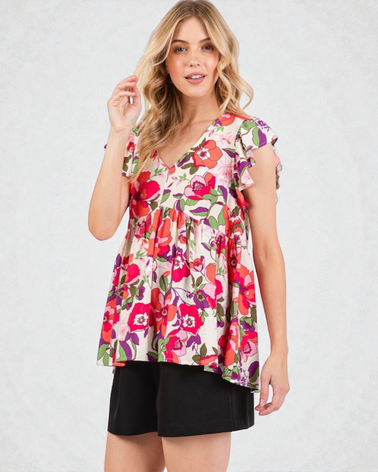 Woman wearing a colorful floral blouse with black shorts on a white background