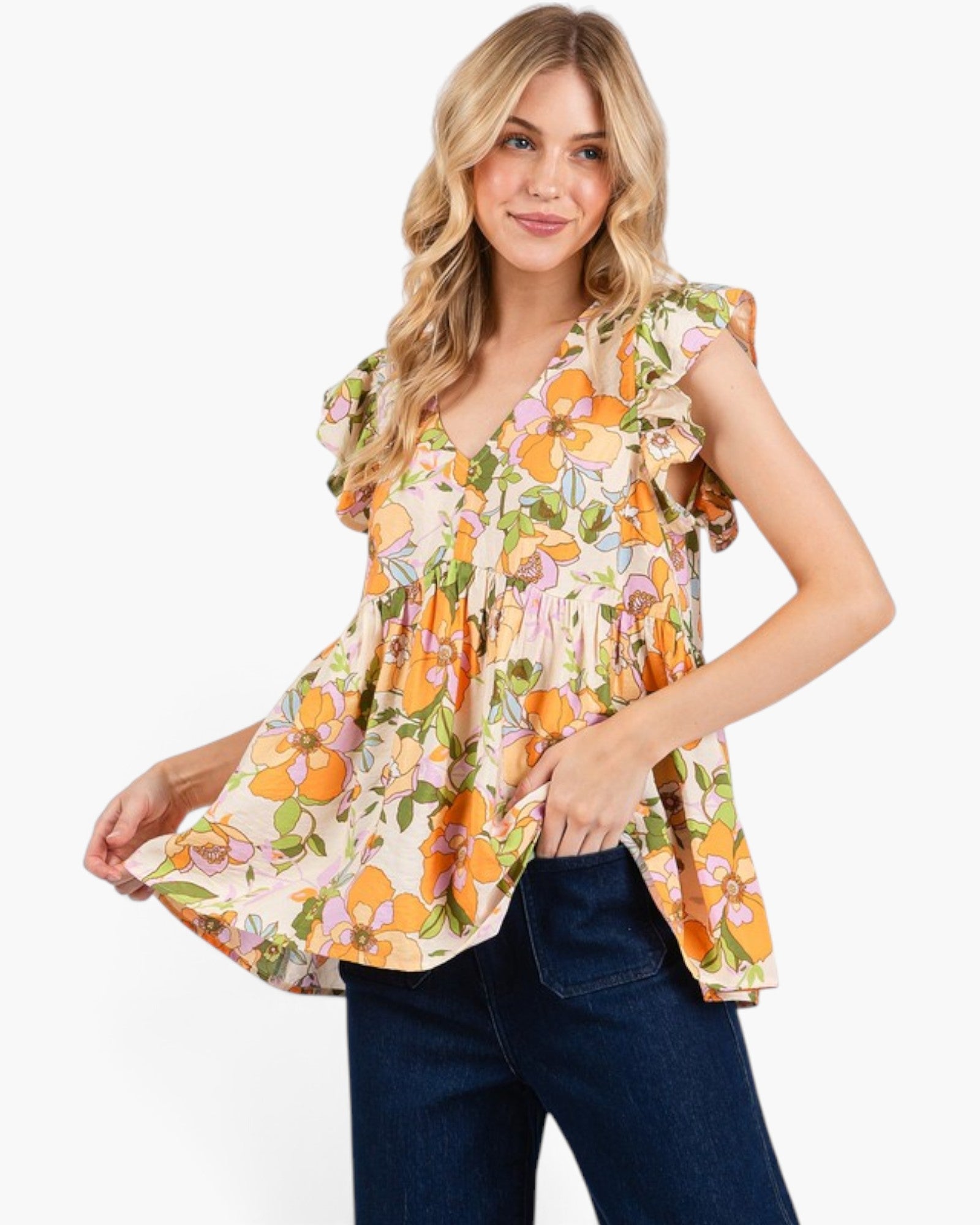 A woman modeling a sleeveless peplum top with a vibrant orange, yellow, and green floral print on a cream background, paired with dark blue jeans against a plain white studio background.