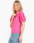 A woman wearing a bright pink textured short-sleeve top with puff sleeves and light blue jeans, photographed against a clean white background.