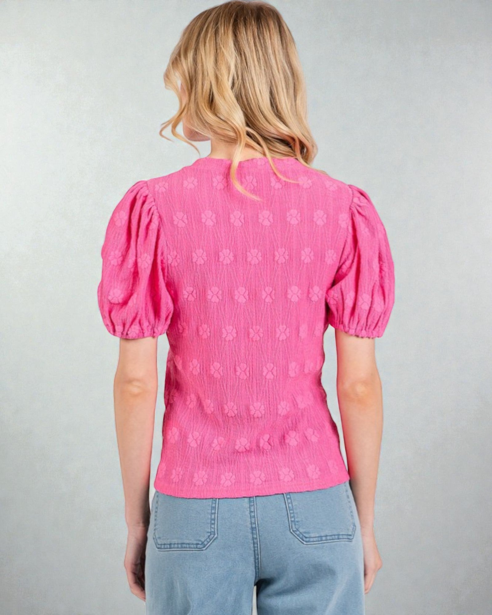 Person wearing a pink blouse with puff sleeves on a gray background