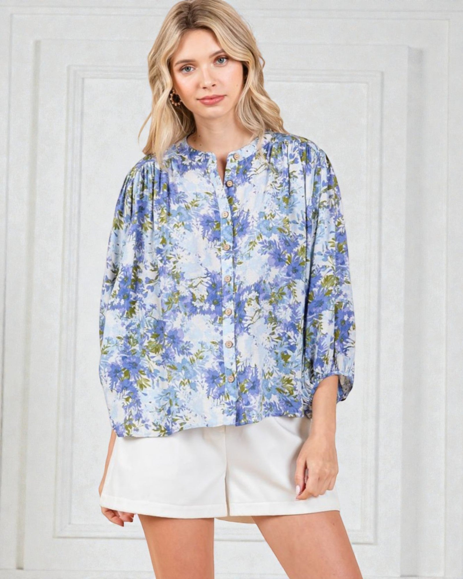 Woman wearing a blue floral blouse and white shorts against a white background