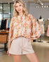 Woman wearing a floral blouse and beige shorts in a clothing store.