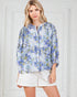 Woman wearing a blue floral blouse and white shorts against a white background