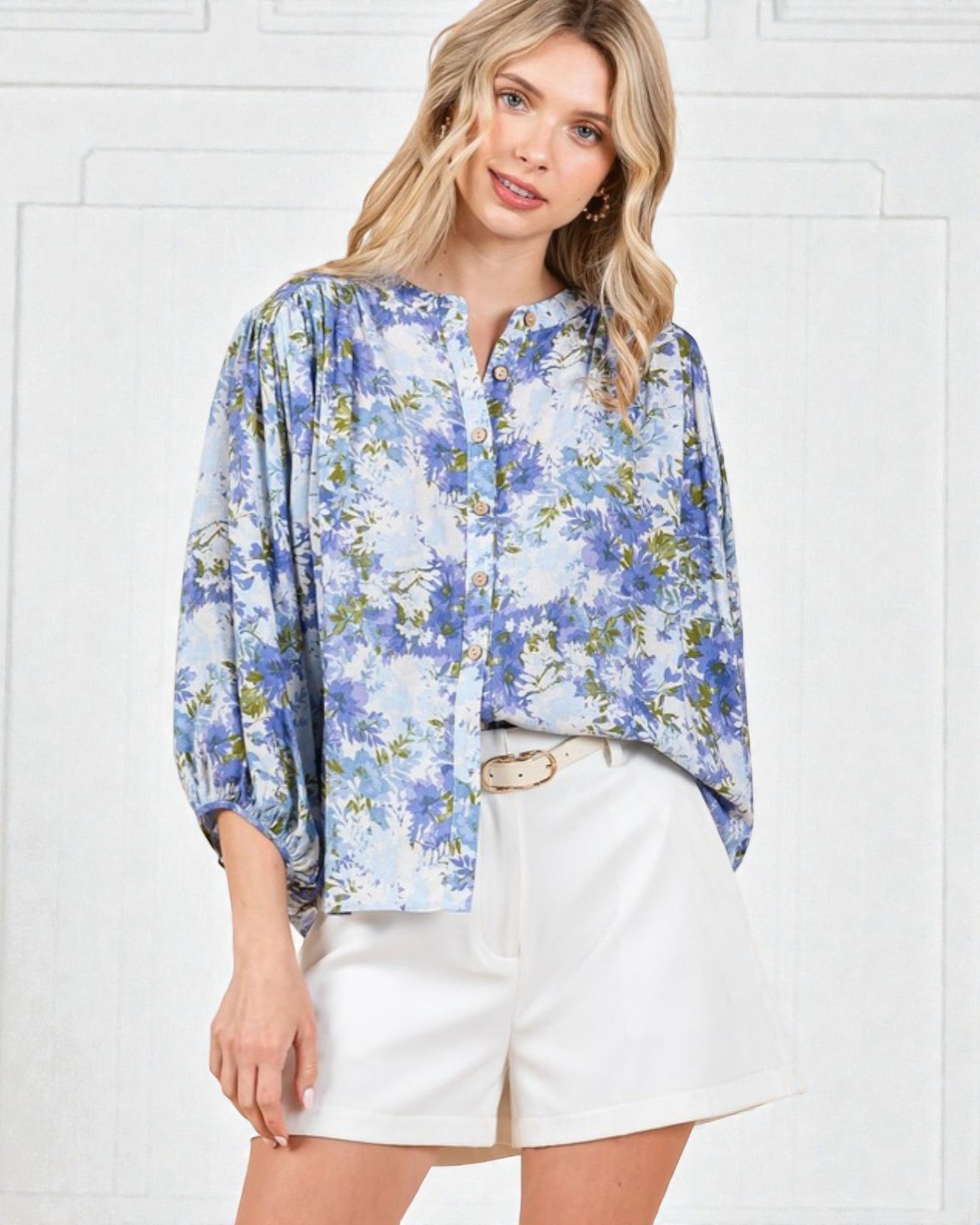 Woman wearing a blue floral blouse and white shorts against a white background