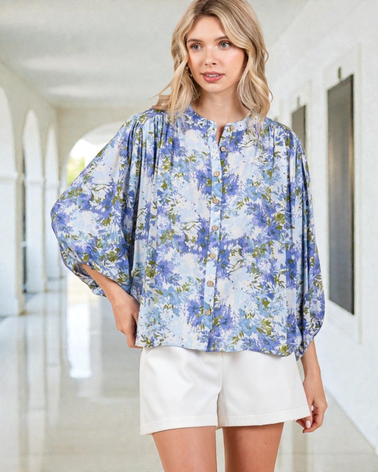 Woman wearing a blue floral blouse and white shorts in an indoor setting