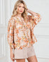 Woman wearing a floral blouse and beige shorts against a white wall