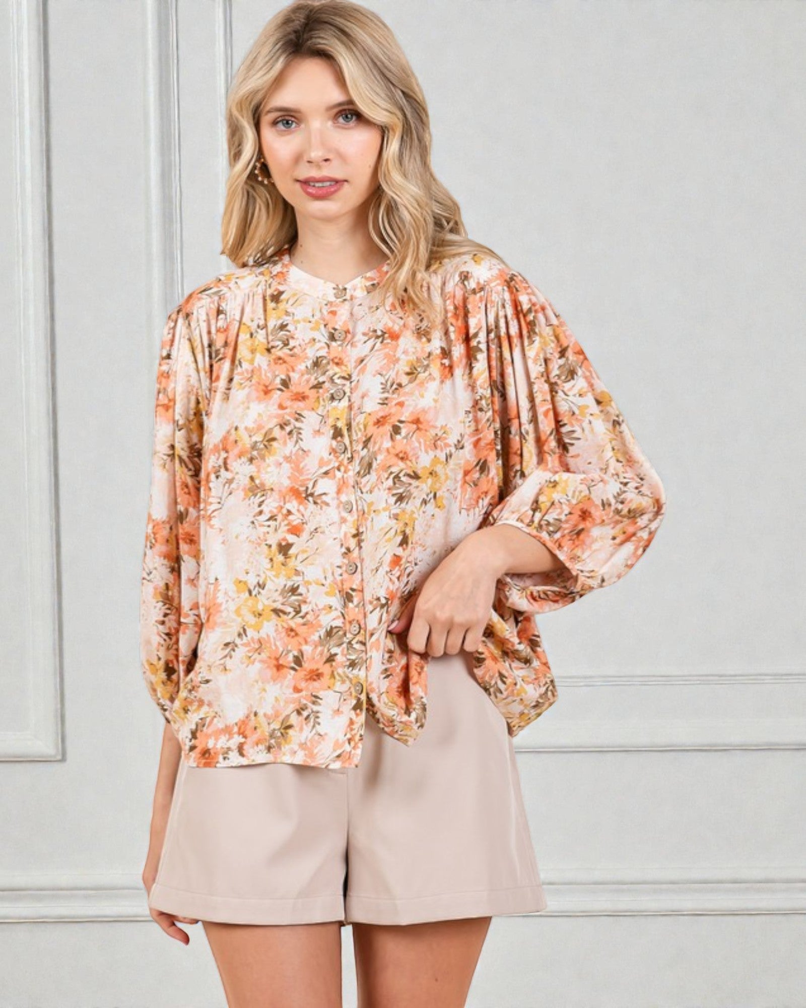 Woman wearing a floral blouse and beige shorts against a light gray background