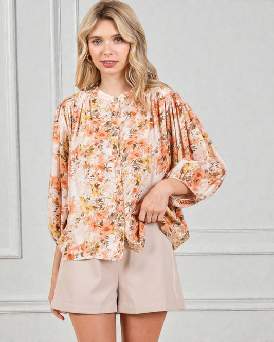 Woman wearing a floral blouse and beige shorts against a light gray background