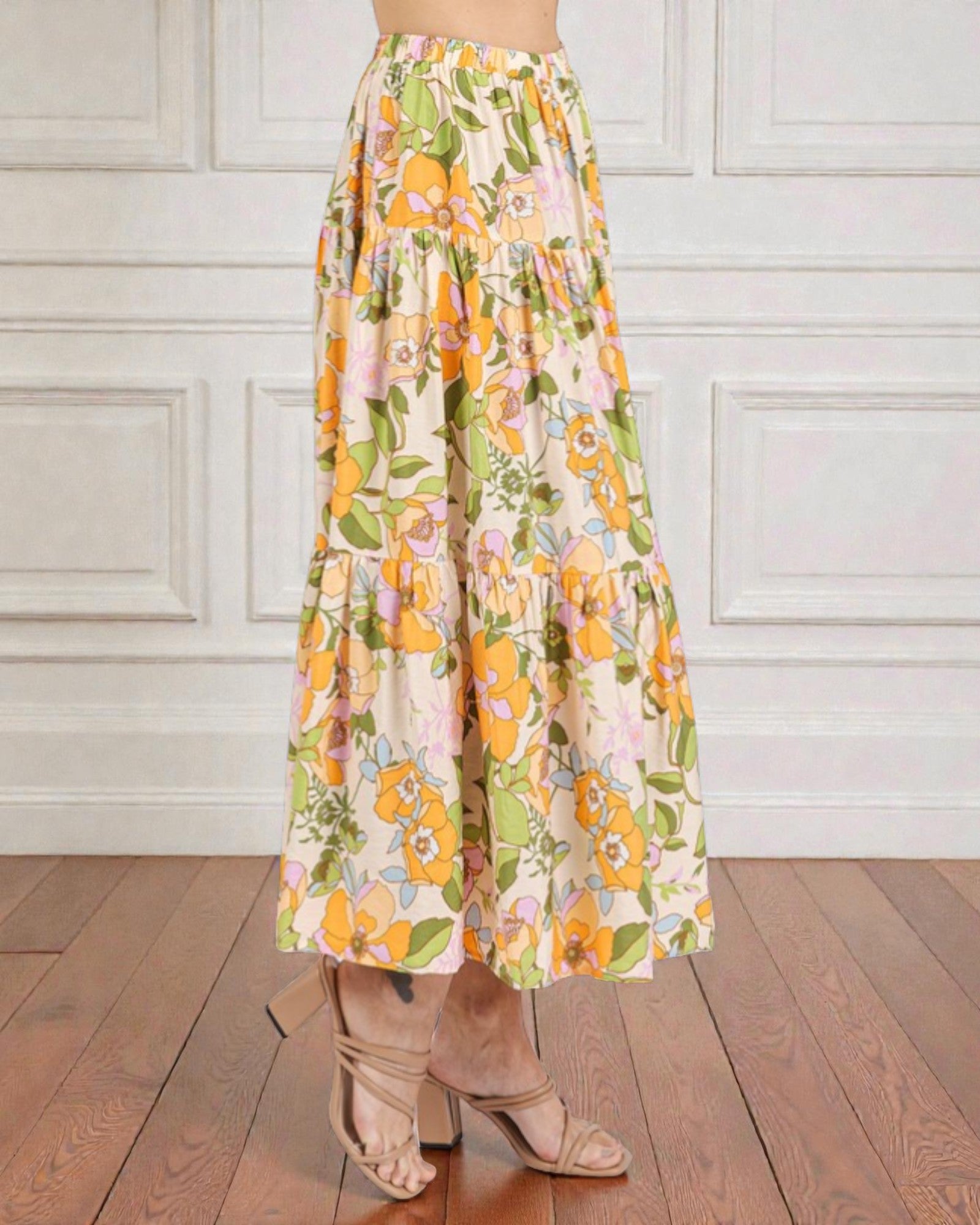 Floral patterned skirt worn by a person on a wooden floor with white paneled walls.