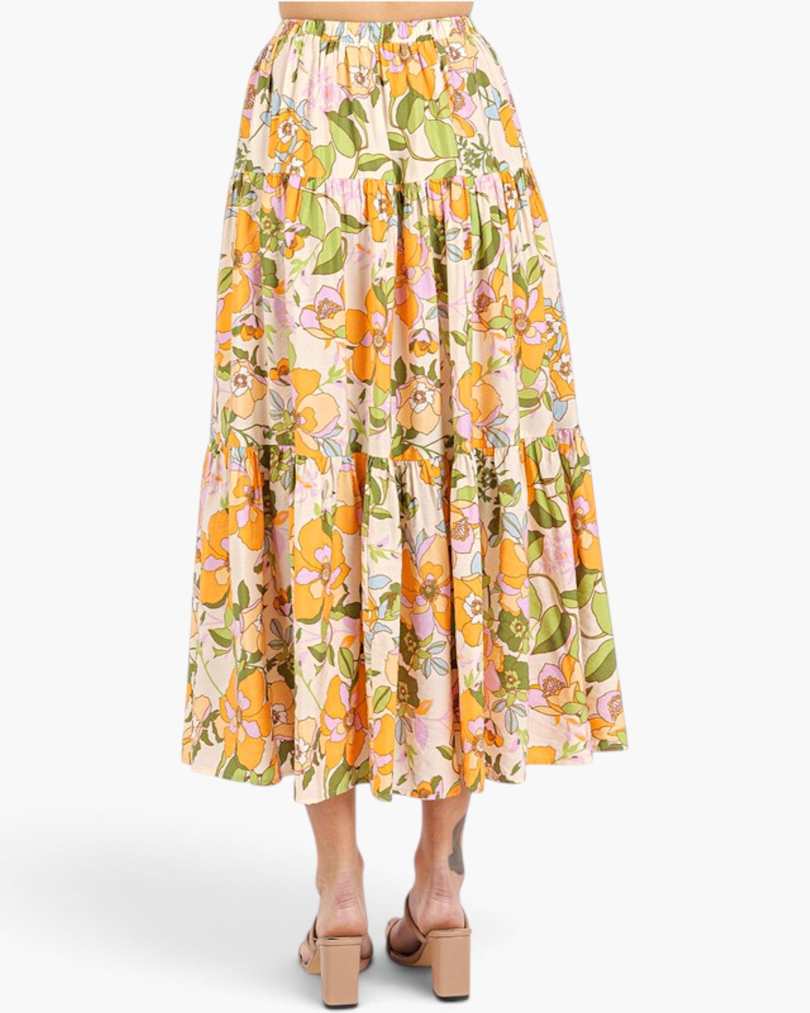 A tiered midi skirt with a vibrant floral print in orange, yellow, pink, and green on a cream background, shown on a model from the back wearing beige block-heel sandals.