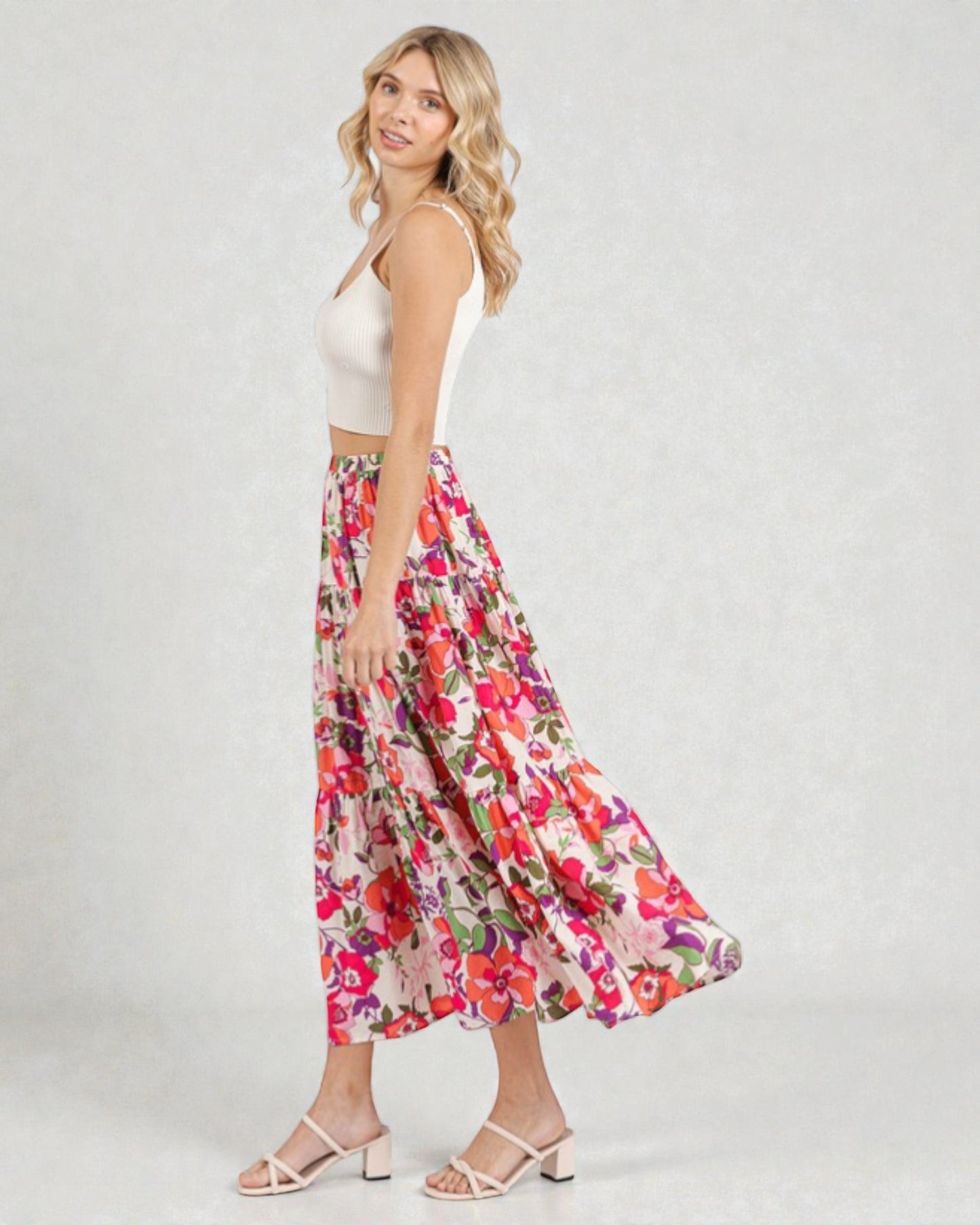 Woman wearing a floral skirt and white top on a plain background