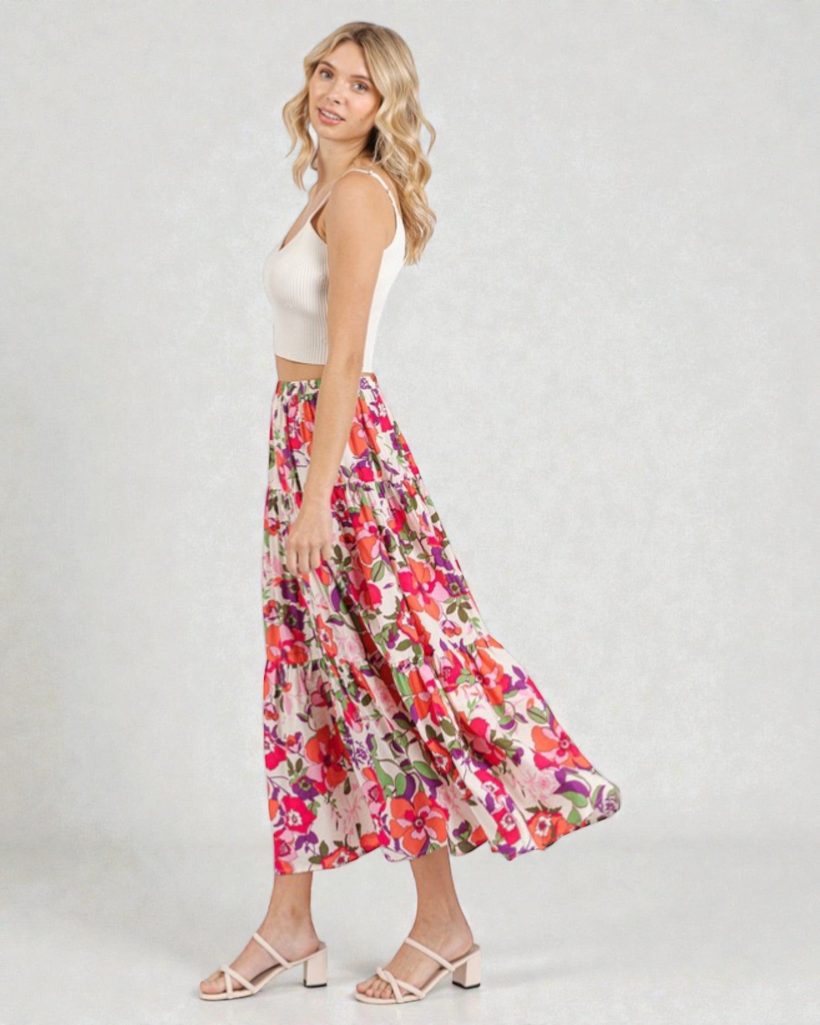 Woman wearing a floral skirt and white top on a plain background