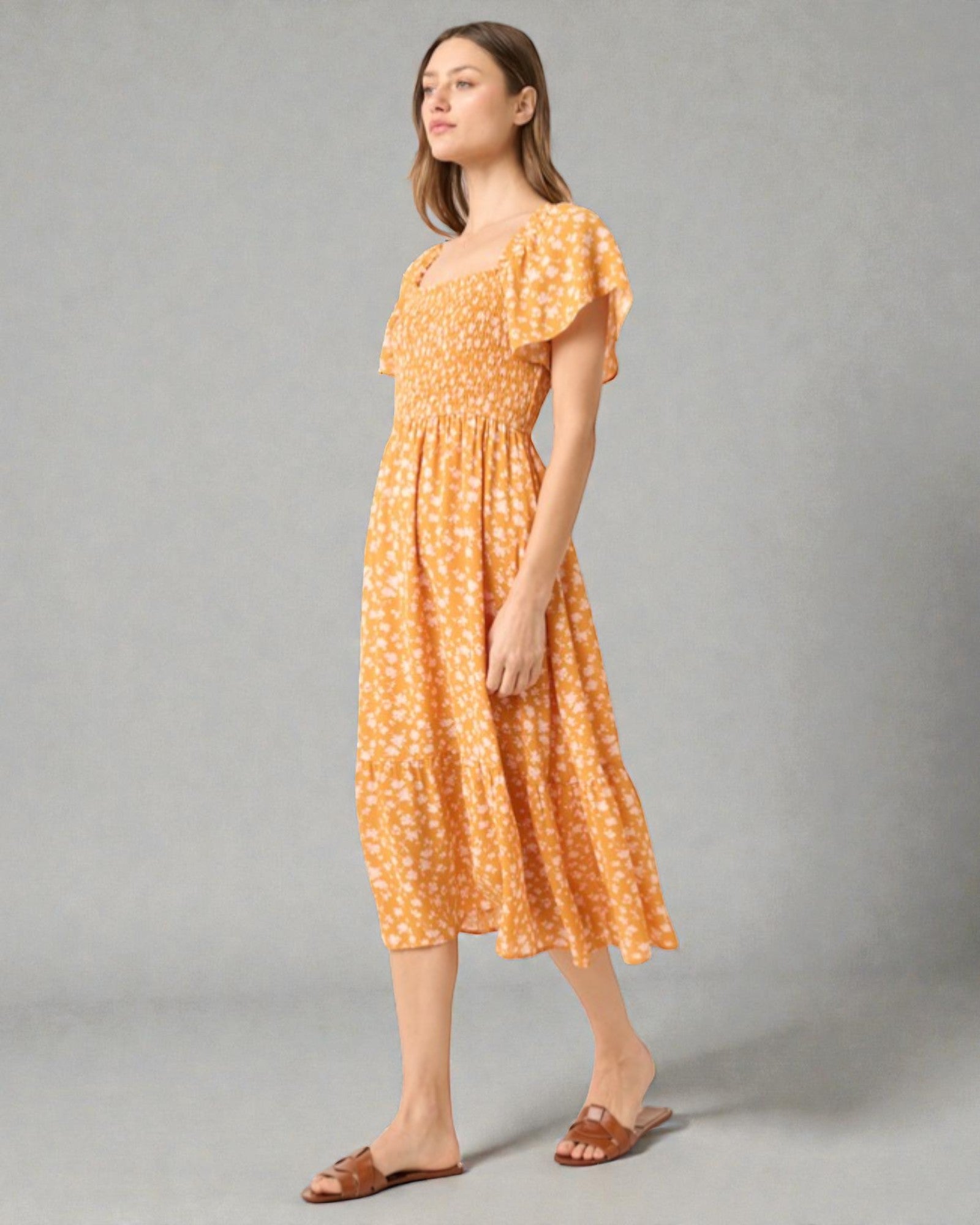 Woman wearing a yellow floral dress against a gray background