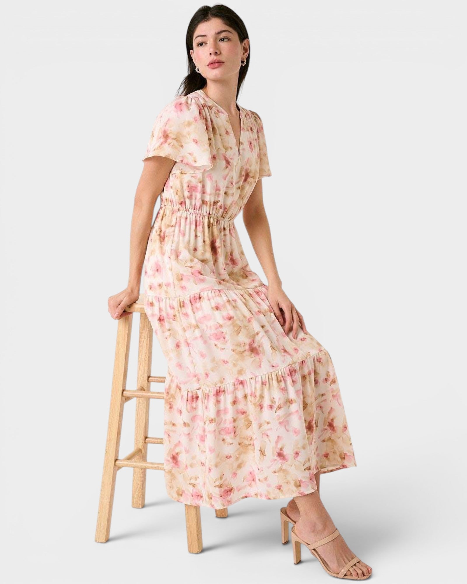 Woman wearing a floral dress sitting on a wooden stool against a white background