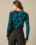 Woman wearing a teal floral long-sleeve top against a beige background