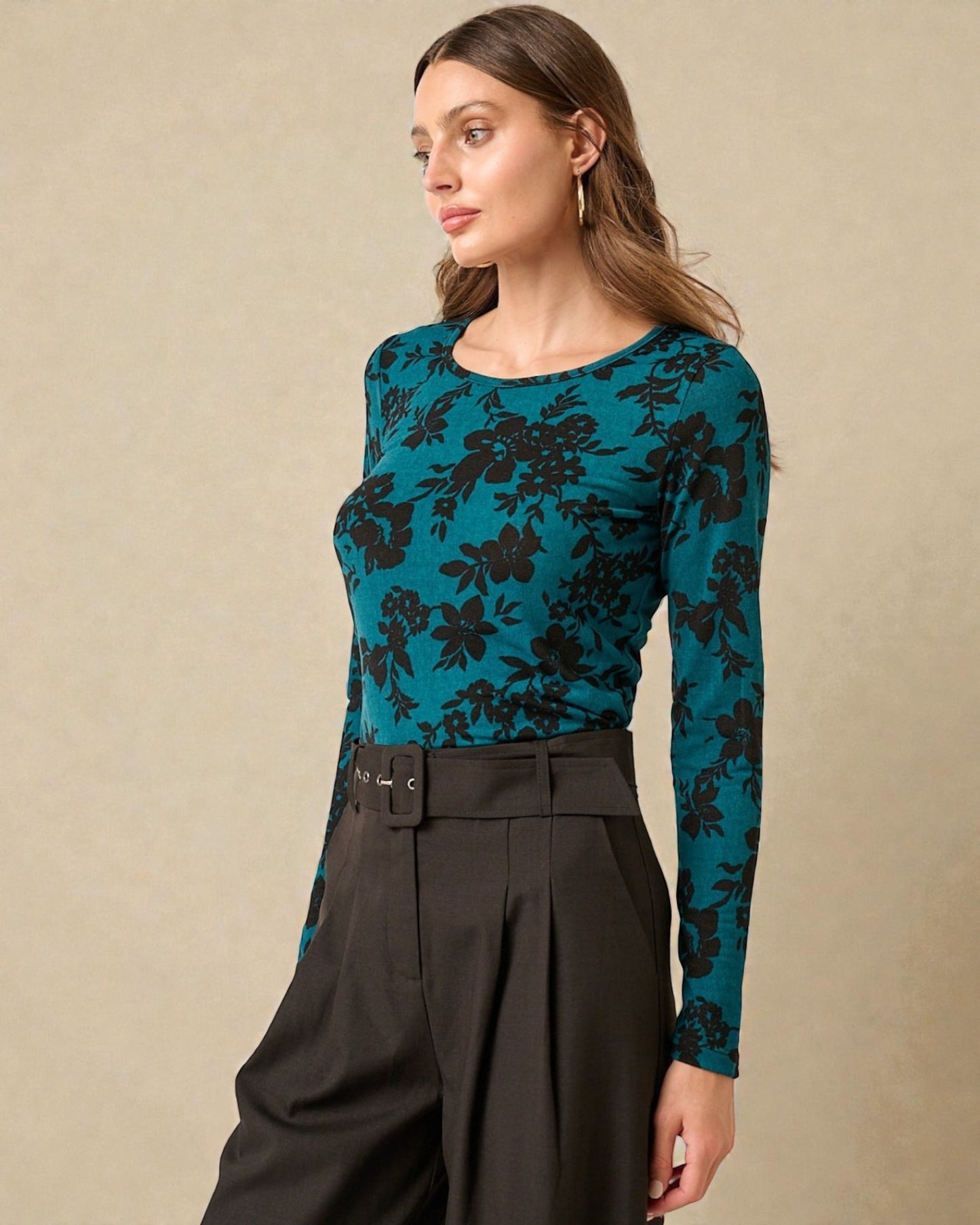 Woman wearing a teal floral long-sleeve top and black pants on a beige background