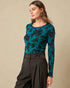 Woman wearing a teal floral long-sleeve top and black pants on a beige background