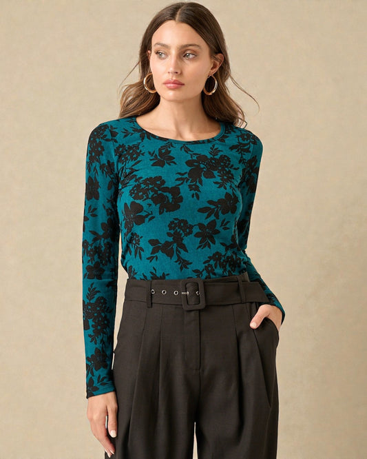 Woman wearing a teal floral long-sleeve top with black pants on a beige background