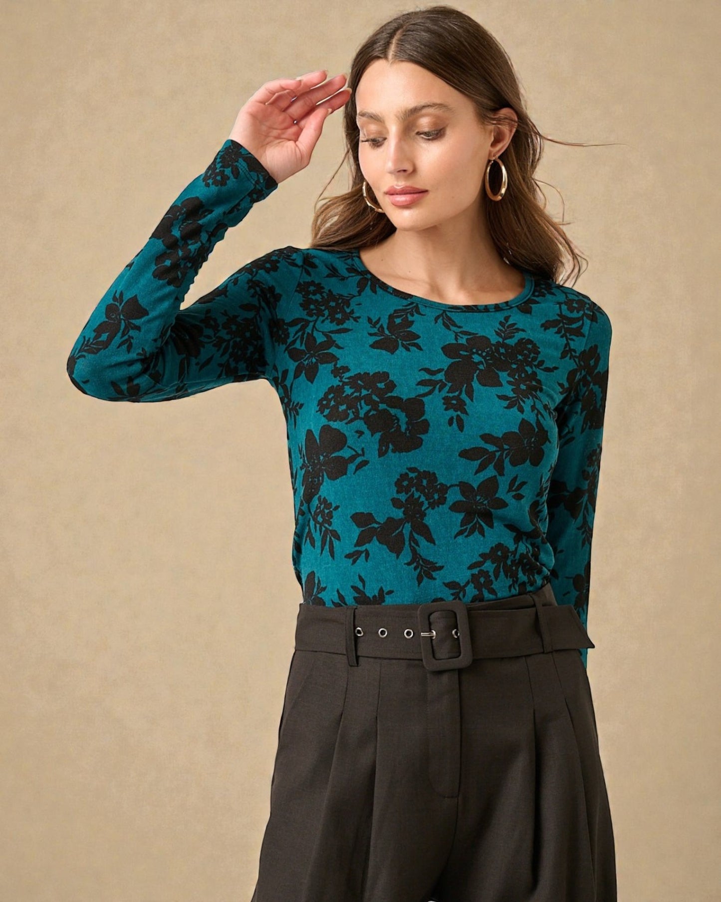 Woman wearing a teal floral long-sleeve top against a beige background